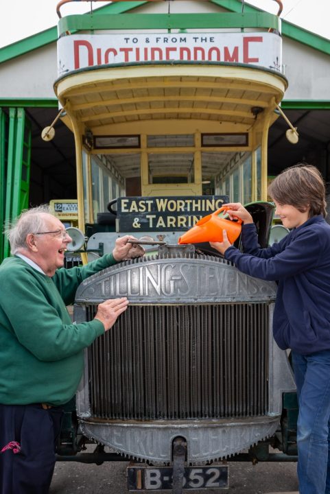 Amberley Museum, Amberley, Sussex, UK, 26th July 2020. After being closed for over 4 months during the Covid-19 crisis, Amberley Museum has opened its doors to families and visitors once again. In Picture: Volunteer bus crew member Alan Lambert gets some help from his nine-year-old grandson, Charlie, to fill up the radiator of a 1914 Tilling-Stevens open top double deck bus at the museum.