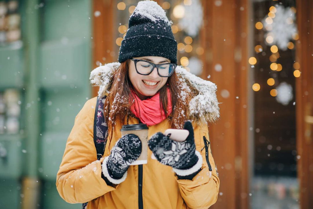 Attractive and cheerful young woman using smartphone in a street. She is checking mails, chats or the news