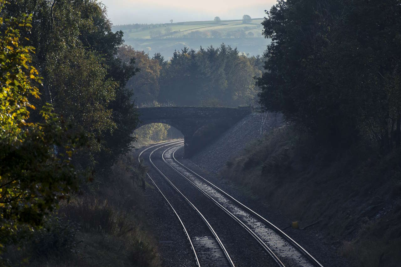 Empty rail track passing beneath a bridge in the English countryside.